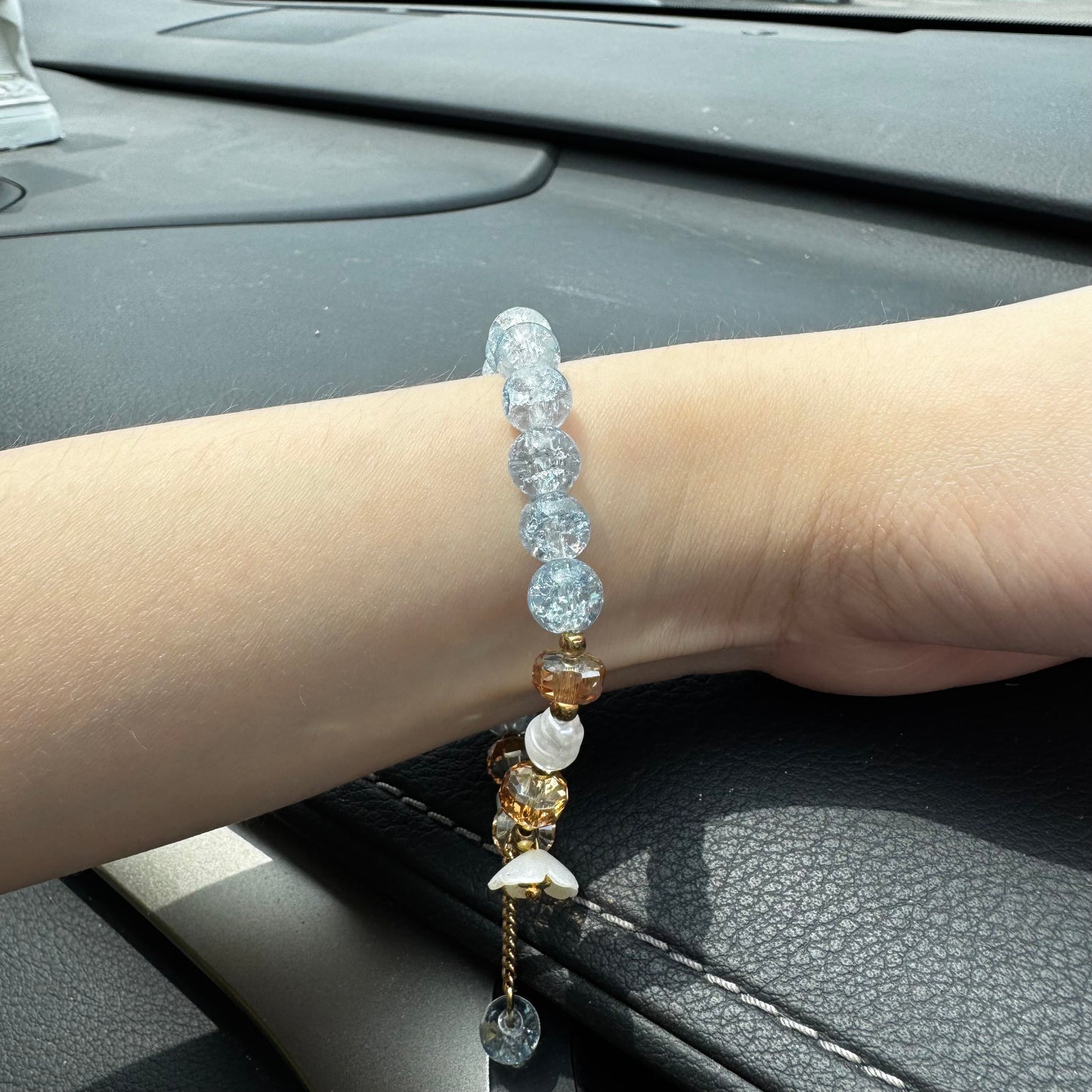 Handmade beaded bracelet with blue crackle beads, white flower charm, and gold crystal accents on hand
