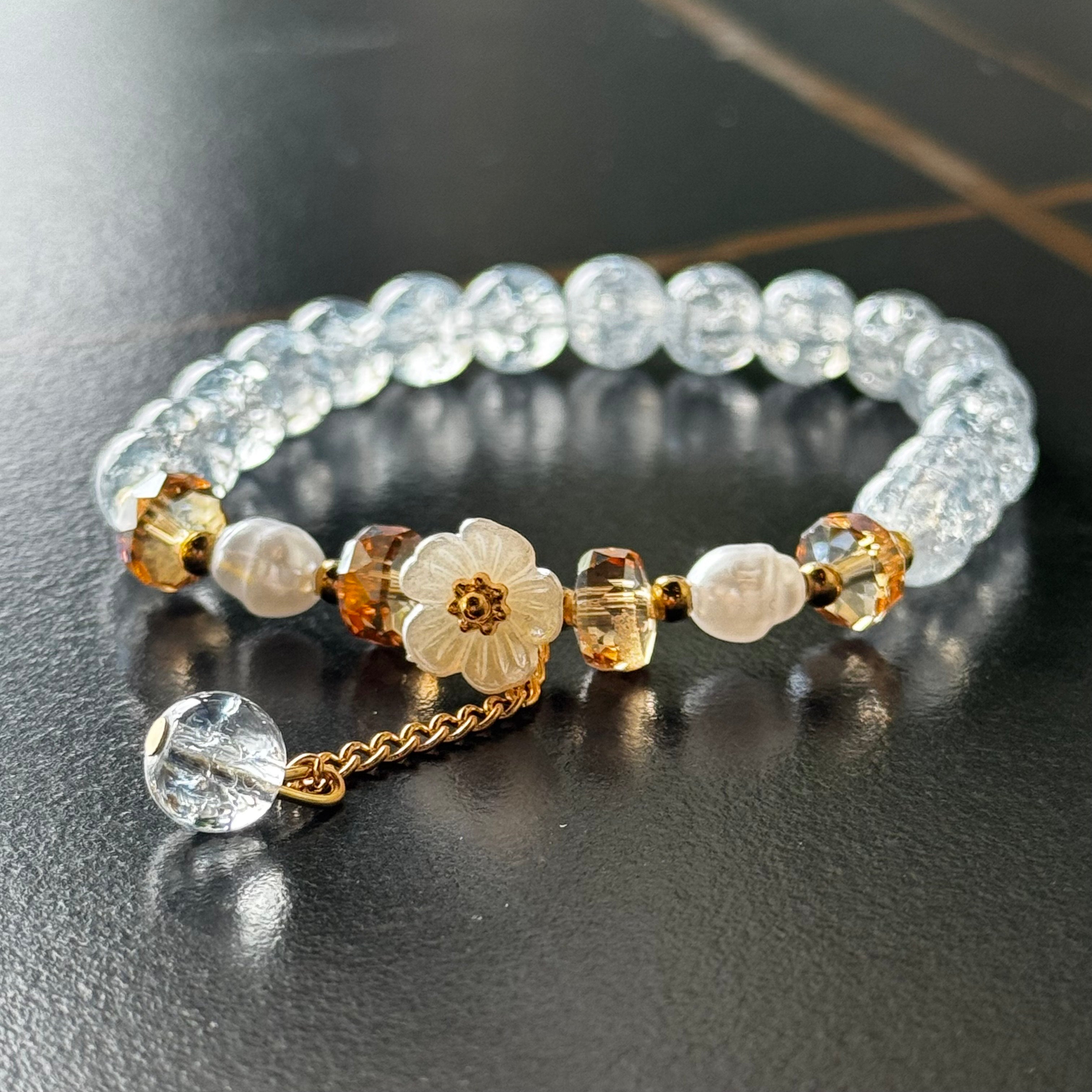 Handmade beaded bracelet with blue crackle beads, white flower charm, and gold crystal accents on a beige box
