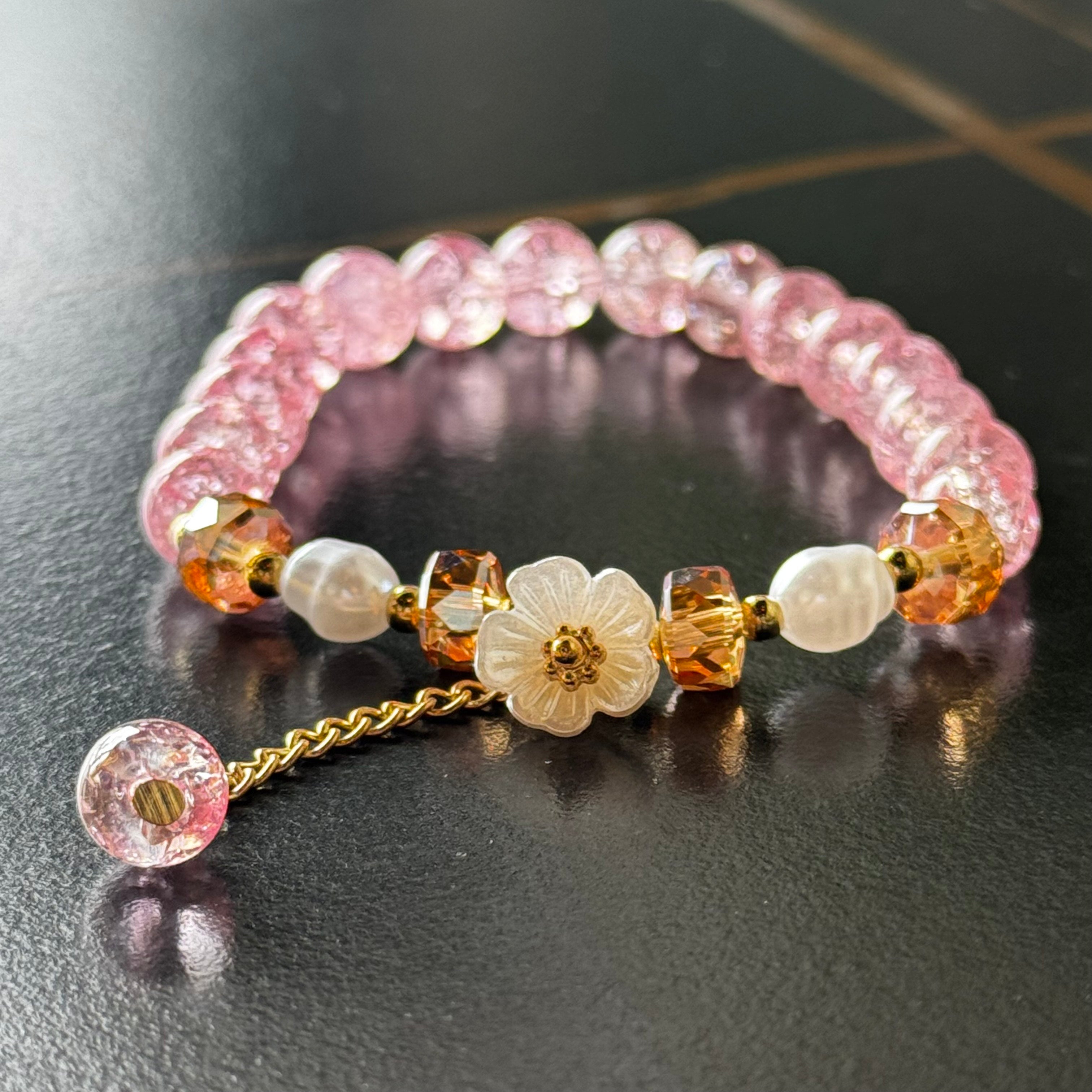Handmade pink crackle beaded bracelet with white flower charm, gold crystals, and dangling bead, displayed in a gift box
