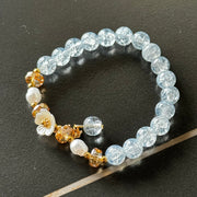 Handmade beaded bracelet with blue crackle beads, white flower charm, and gold crystal accents on a beige box