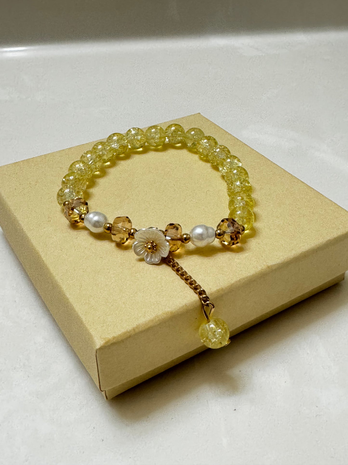 Handmade yellow crackle glass bracelet with white flower charm, pearl accents, and gold crystal beads, styled in a gift box on white background