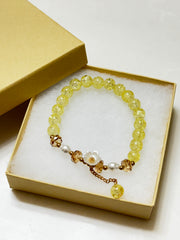 Handmade yellow crackle glass bracelet with white flower charm, pearl accents, and gold crystal beads, styled in a gift box on white background