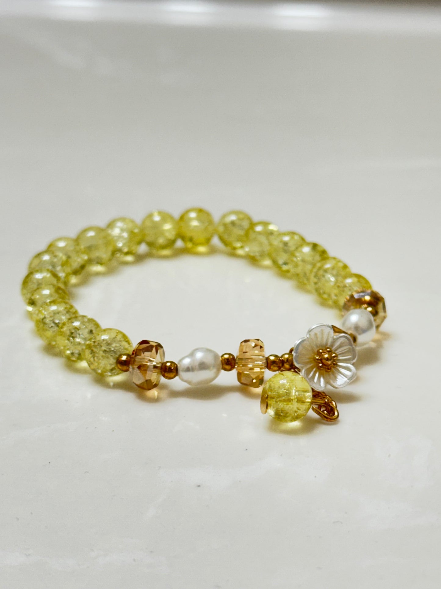 Handmade yellow crackle glass bracelet with white flower charm, pearl accents, and gold crystal beads, styled in a gift box on white background