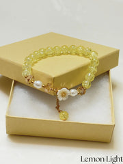 Handmade yellow crackle glass bracelet with white flower charm, pearl accents, and gold crystal beads, styled in a gift box on white background