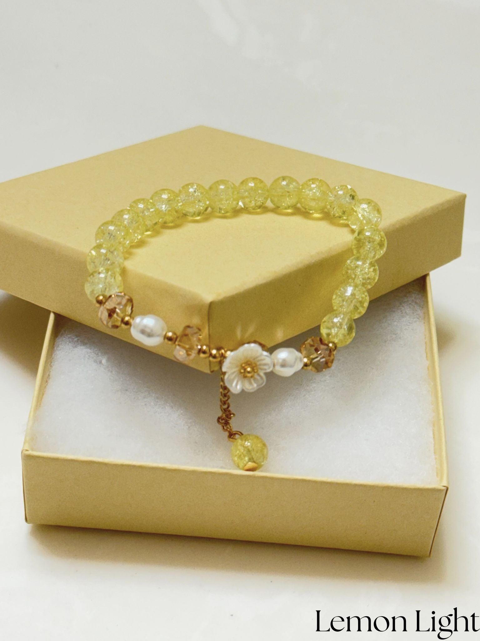 Handmade yellow crackle glass bracelet with white flower charm, pearl accents, and gold crystal beads, styled in a gift box on white background